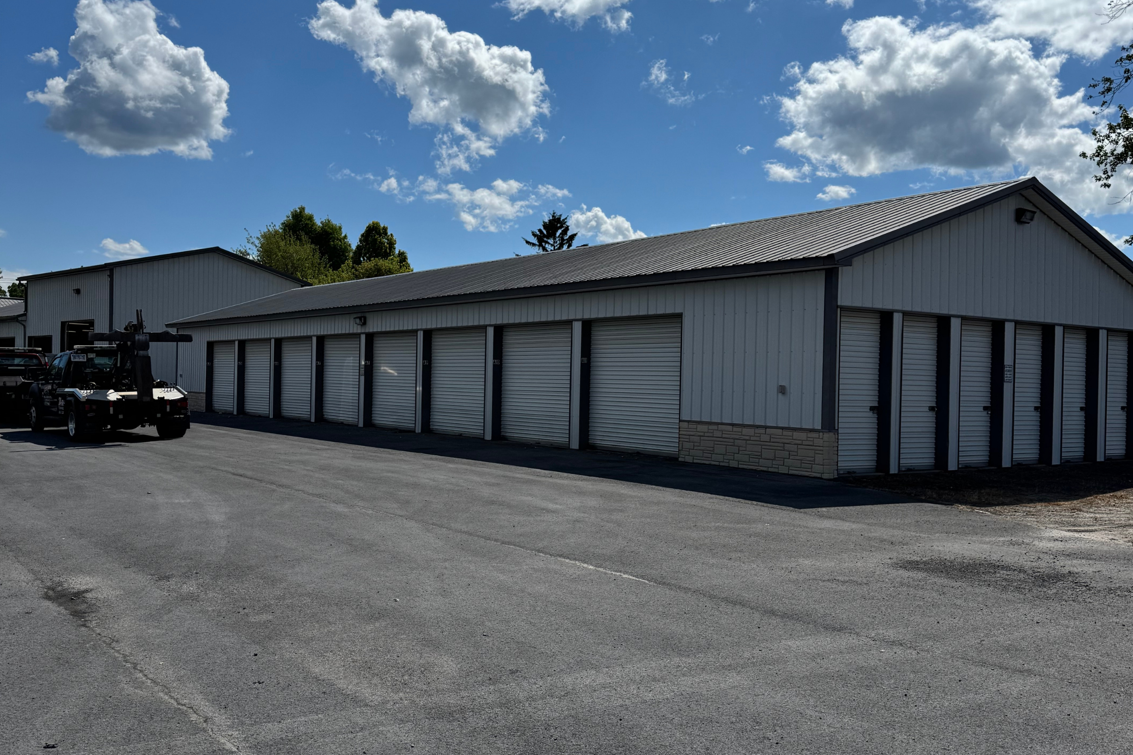 Storage facility with multiple roll-up door units, paved driveway, and parked service trucks in front of one building.